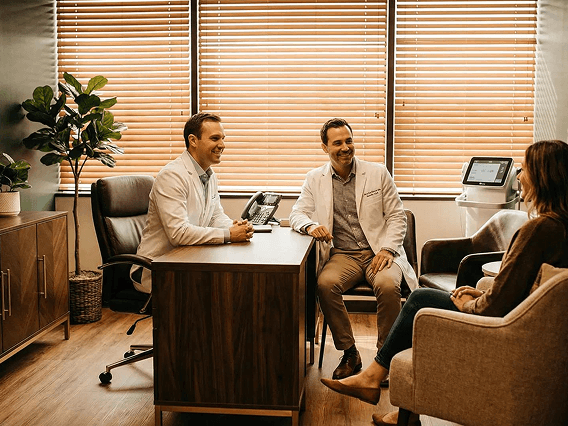Medical consultation at AH Clinics with two healthcare professionals discussing personalized Glow Peptide therapy with a patient in a modern office setting.